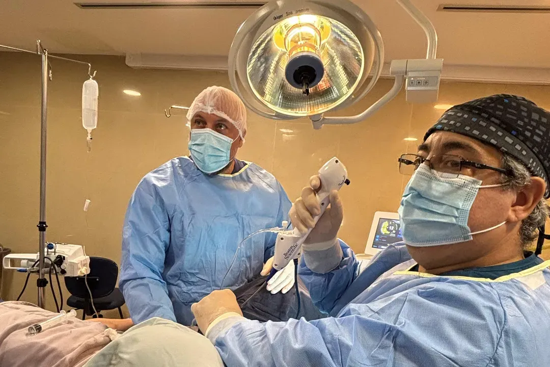 Dos cirujanos en quirófano bajo la lámpara quirúrgica, uno de ellos con un endoscopio en la mano