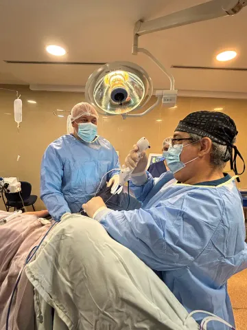 El equipo quirúrgico en el quirófano durante una litotricia, con un cirujano sosteniendo el ureteroscopio bajo la lámpara
